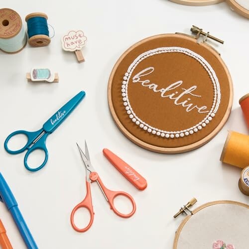 Flatlay of embroidery tools and scissors around an embroidery hoop.