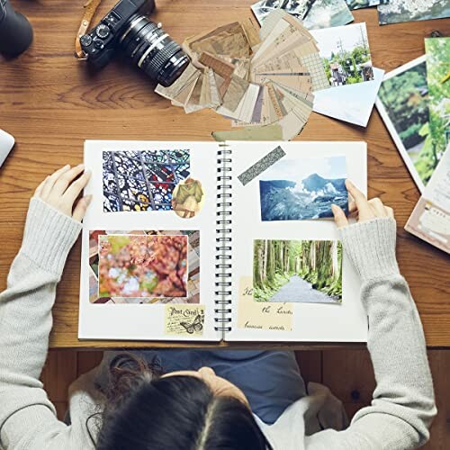 Person scrapbooking with photos and camera on table.